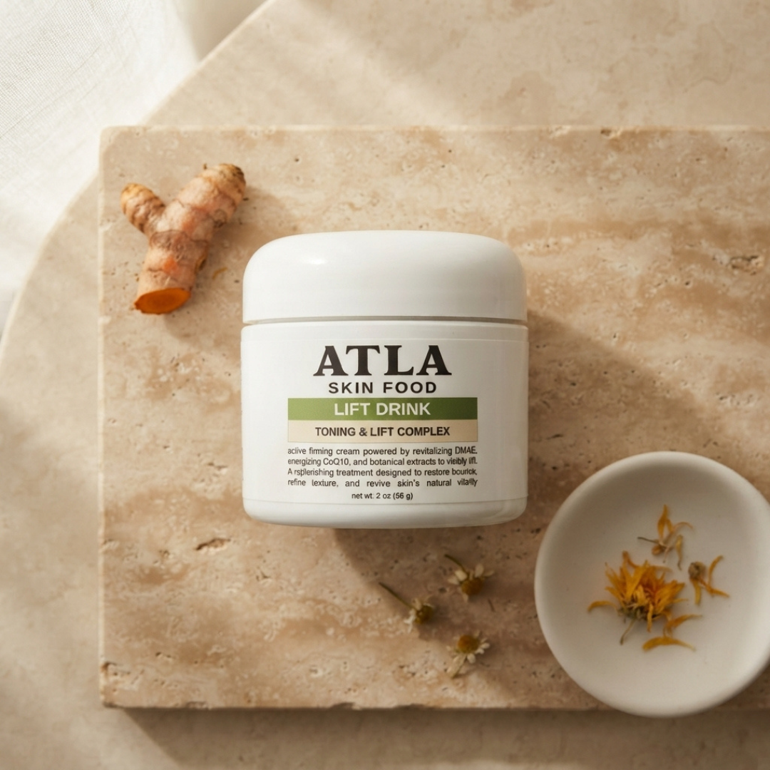 ATLA Skin Food Lift Drink Toning & Lift Complex cream jar, styled on a beige stone slab with ginger root, dried flowers, and a small dish of ingredients.