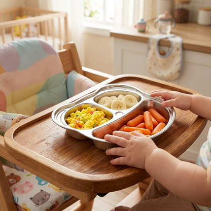 Child in a highchair using a Steely Kids stainless steel divided plate during mealtime.