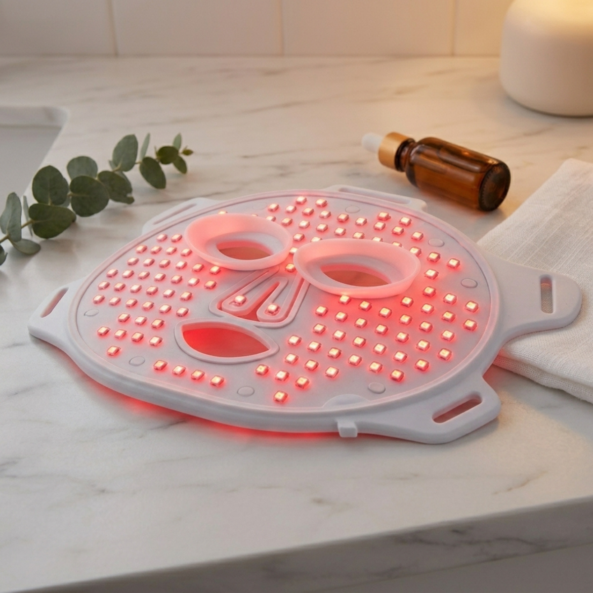 Red light therapy face mask glowing on a bathroom counter beside skincare accessories