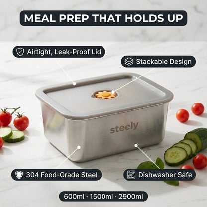 A stainless steel meal prep container with a leak-proof lid and food storage compartment, shown on a light marble surface with tomatoes, cucumber slices, and overlaid feature callouts including 'Meal Prep That Holds Up,' 'Airtight, Leak-Proof Lid,' 'Stackable Design,' '304 Food-Grade Steel,' and 'Dishwasher Safe.'.